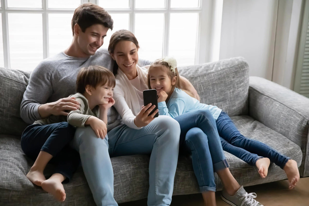 A happy family sharing a phone together on the couch